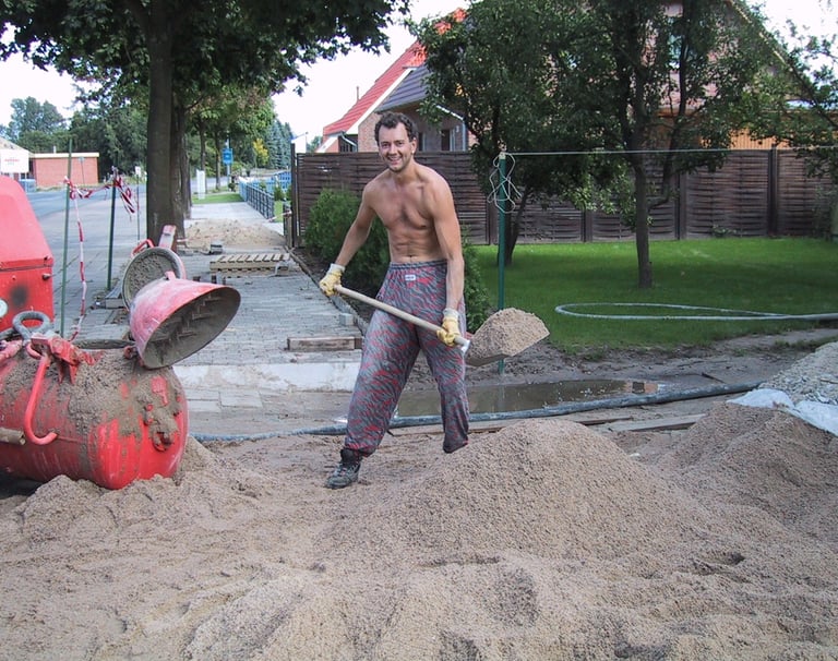 Jörg Grube steht auf der Baustelle und schaufelt Sand in den Botonmischerr