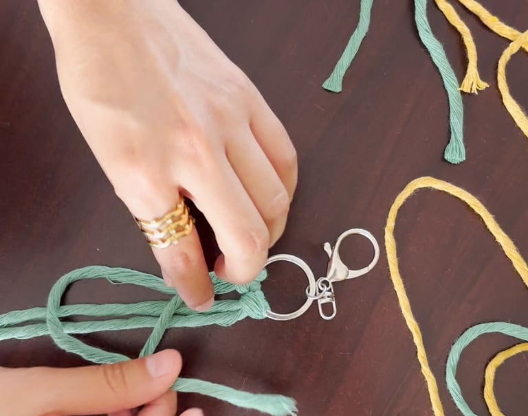 manos tejiendo un llavero de maramé azul y cordones de colores sobre la mesa de trabajo