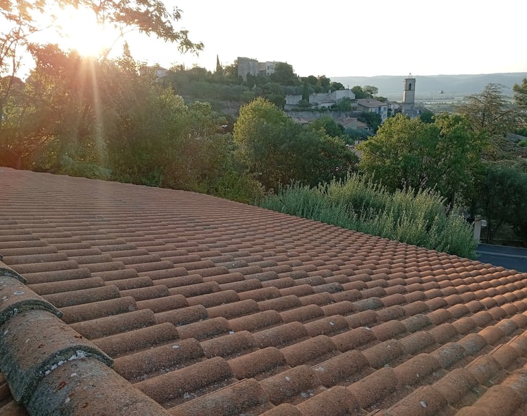 Vue sur une toiture traditionnelle à Volx (Alpes-de-Haute-Provence) avec en arrière-plan le village et son clocher, futur sit
