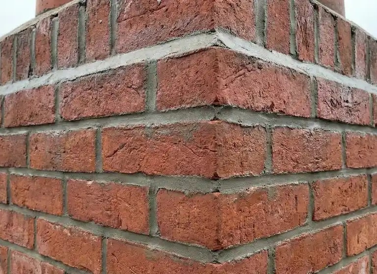 Close-up of a red brick chimney with fresh mortar repointing on a residential rooftop.