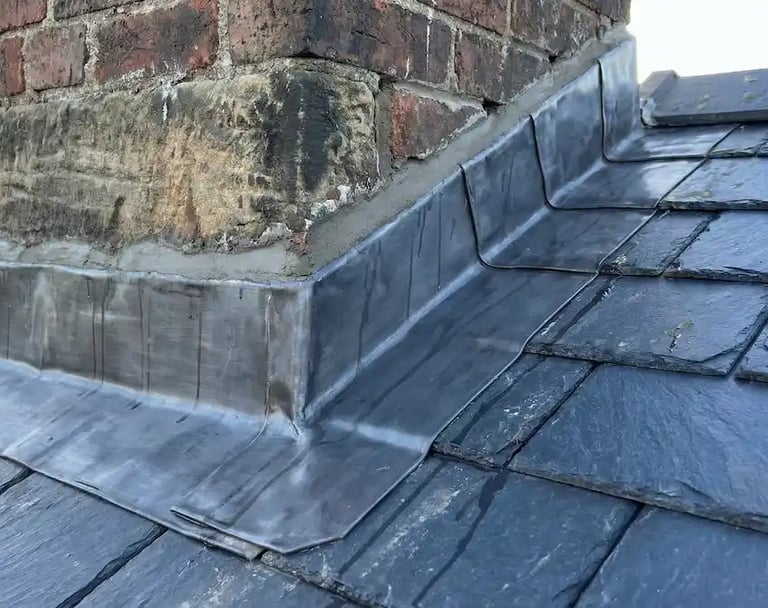Professional lead flashing installation around a brick chimney on a grey slate roof.
