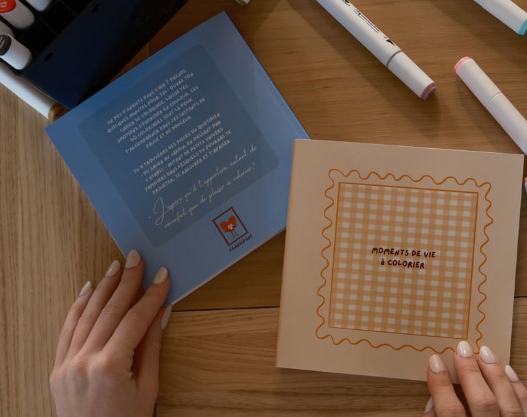 mains feuilletant un livre de coloriage posé sur une table avec feutres