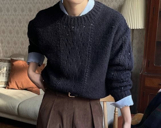 a man in a sweater and pants standing in front of a table
