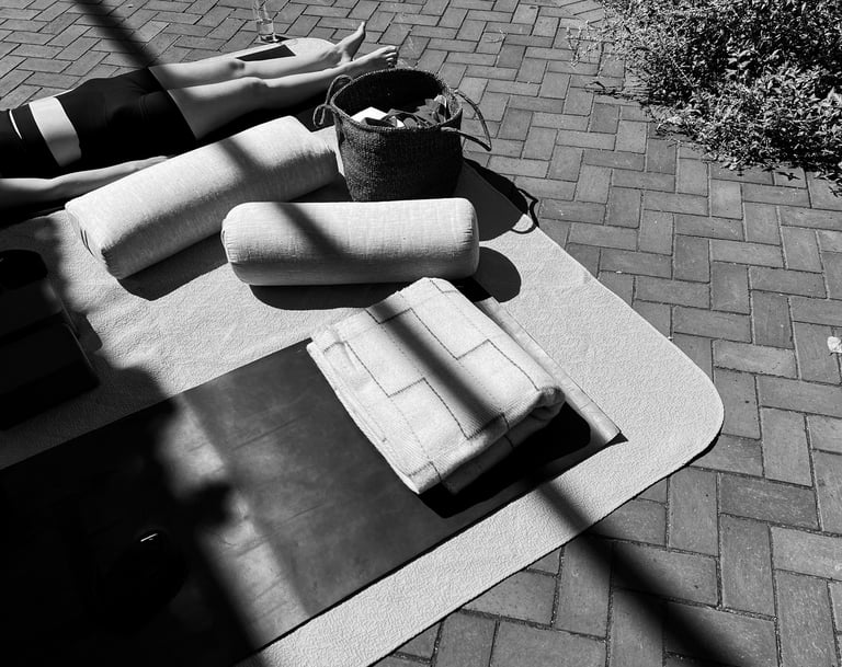 Black and white image of an outdoor Personalized Yoga session with a client in savasana, surrounded by bolsters and props