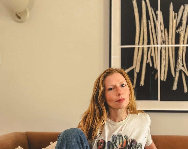Editorial portrait of a yoga teacher with red hair and somatic practitioner, seated on a sofa. 