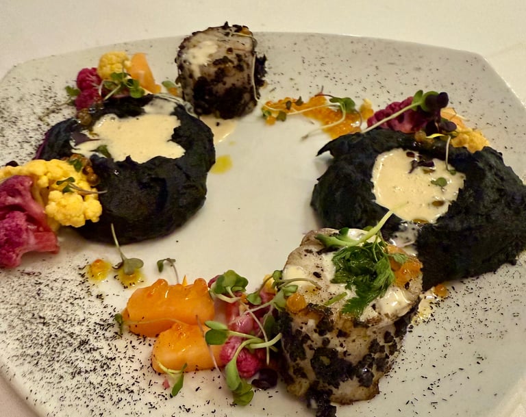 Gourmet plated fish with black squid ink puree, colorful cauliflower, and creamy sauce.