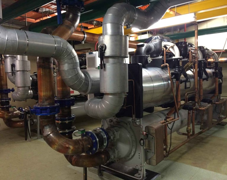 Industrial HVAC chiller system with insulated steel pipes and copper plumbing in a plant room.