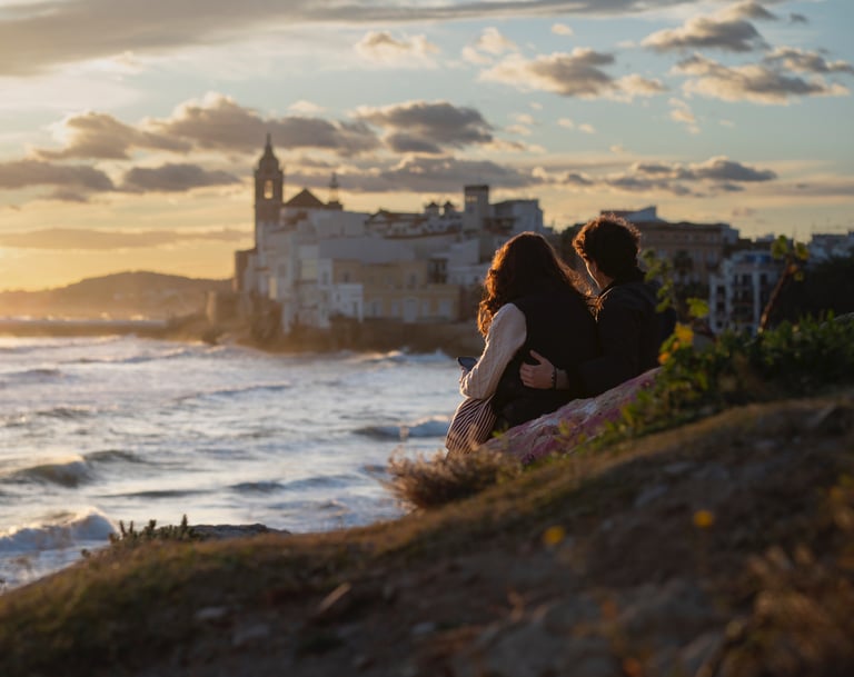 Couple watching a golden sunset over the Sitges coastline and Mediterranean Sea in Spain.