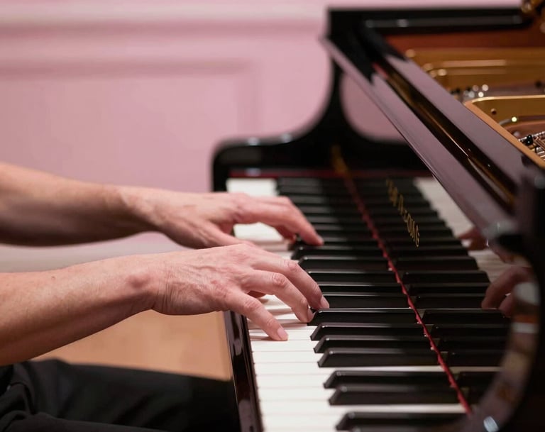 Elegant hands of a musician playing a grand piano in a prestigious North American / US concert hall. The lighting is a gentle mist of soft pink, highlighting the polished wood and the delicate, graceful movement of the fingers.