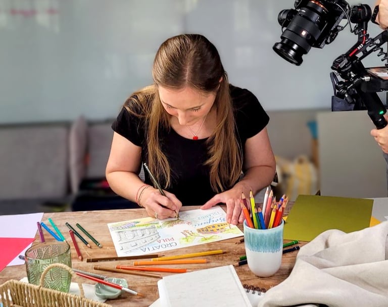 An artist drawing a Croatia travel illustration with colored pencils while being filmed by a professional camera.