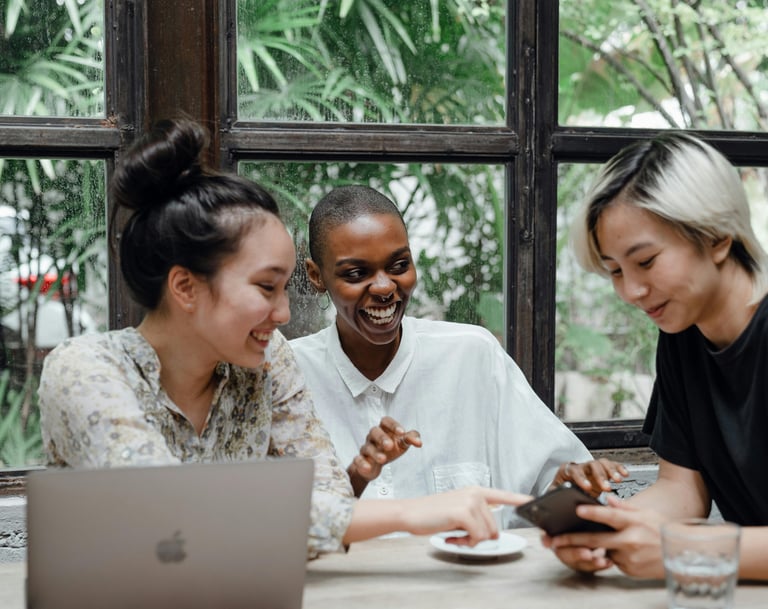 three people sitting at a table with a laptop having a conversation