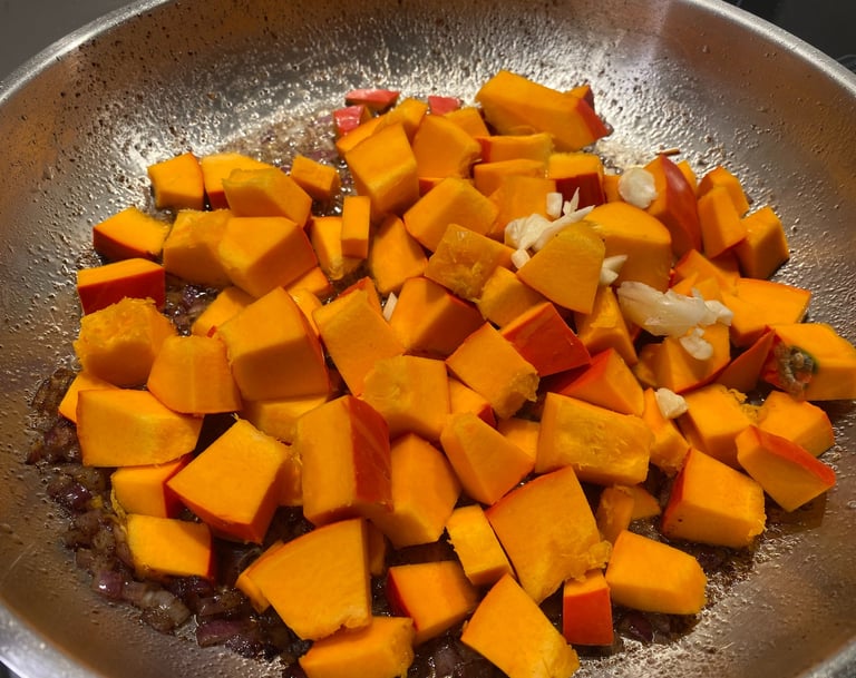 Diced pieces of fresh Hokkaido pumpkin being sautéed in a stainless steel pan with onions.