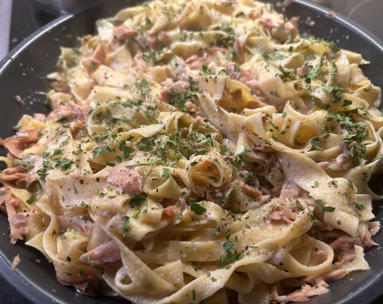 Creamy salmon tagliatelle pasta seasoned with fresh herbs and black pepper in a pan.