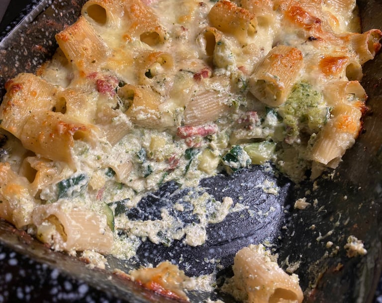 Baked rigatoni pasta with melted cheese, broccoli, and creamy white sauce in a baking dish.