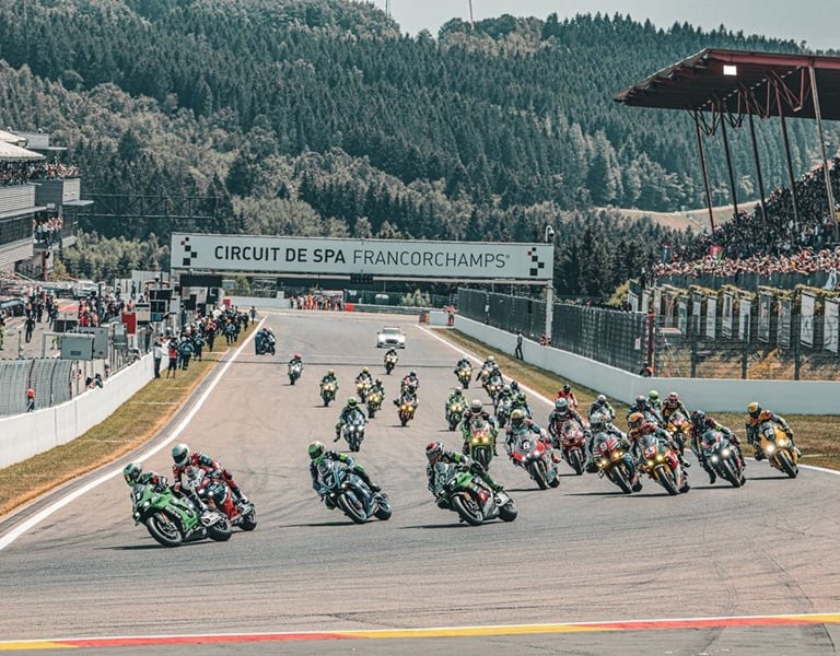 Des pilotes de moto en pleine course sur un circuit, avec un public en arrière-plan