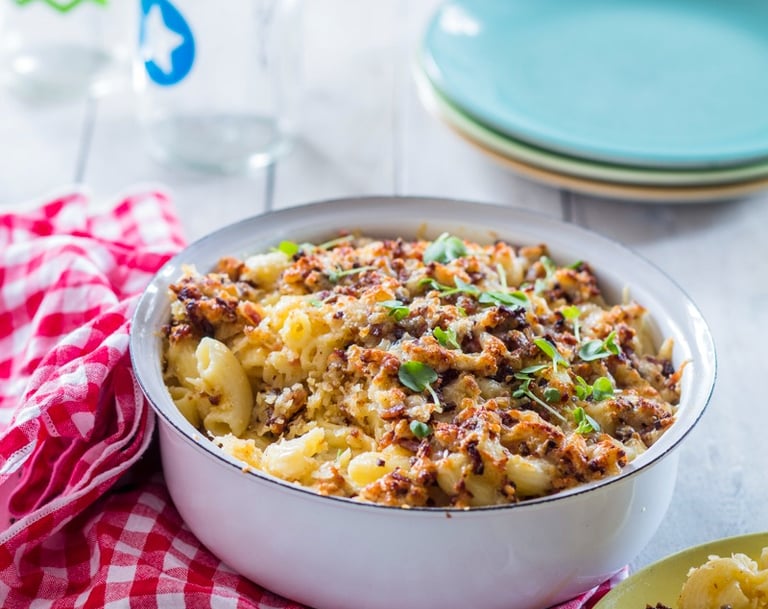 Mac n Cheese with a crunchy topping in an enamel bowl with serving plates to the rear and a napkin