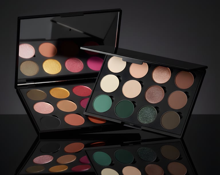 Professional eyeshadow palettes with colorful matte and shimmer pans on a reflective black surface.
