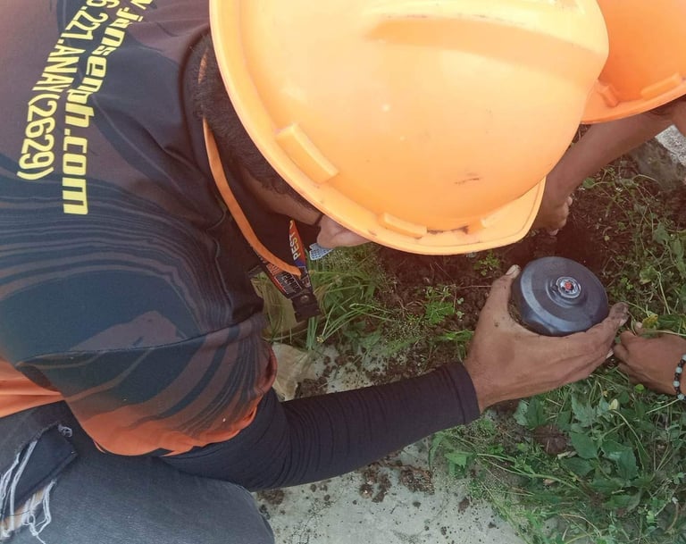 A pest control technician in a hard hat installs an underground termite bait station in soil.
