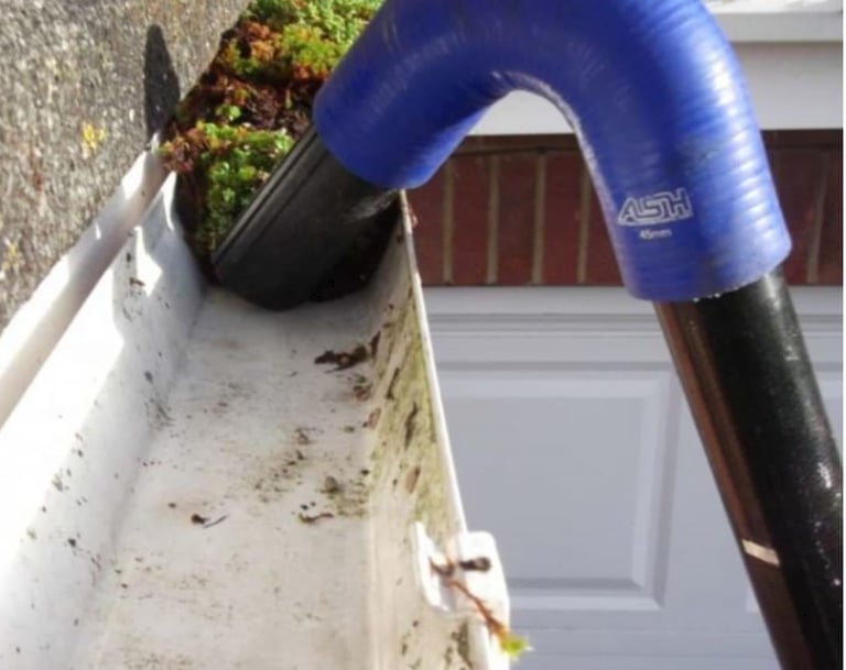 A curved gutter vacuum attachment cleaning debris and moss from a white residential gutter system.