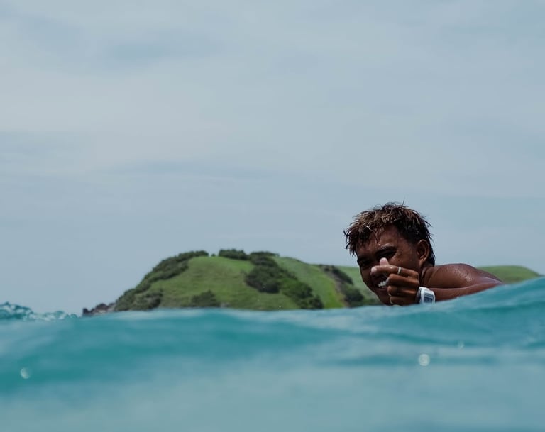 A smiling surfer giving a heart up in turquoise ocean water in Tanjung Aan