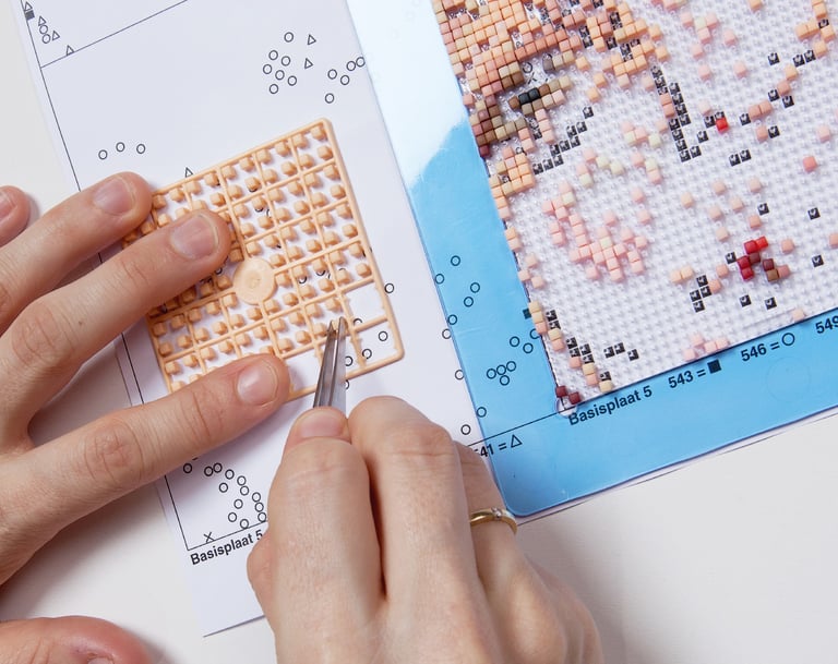 Human creating a picture by using tweezers, transparent baseplate and colorful pixel squares