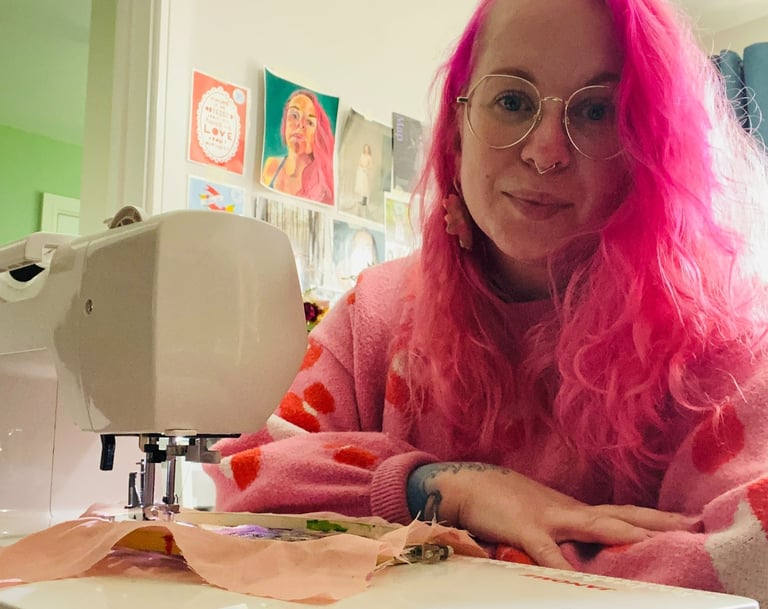 Harriet Mee, a woman with pink hair and glasses on a table next to a sewing machine