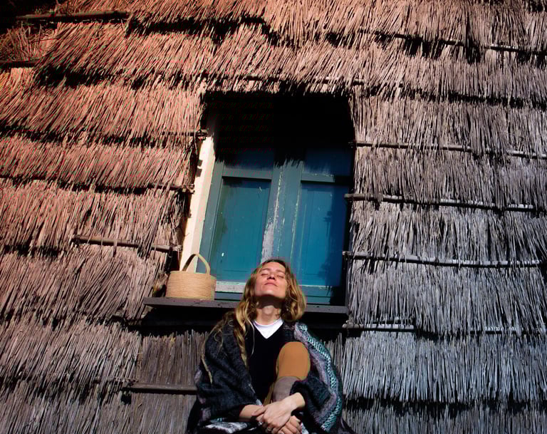 a woman sitting in front of ancient sardinian house on the seaside