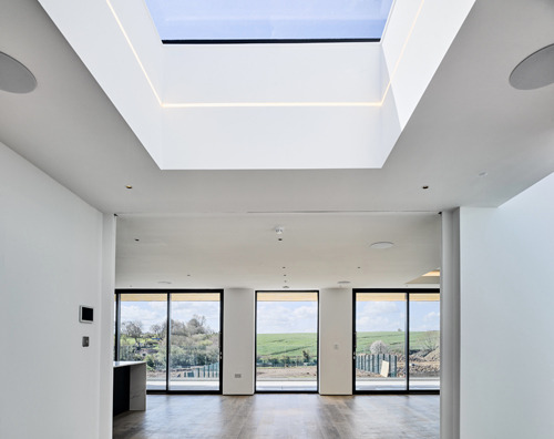 Modern white interior featuring a large rectangular skylight and sliding glass doors with a countryside view.