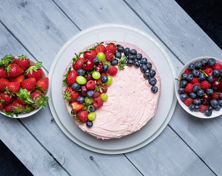 a cake with fruit on a table with bowls of fruit