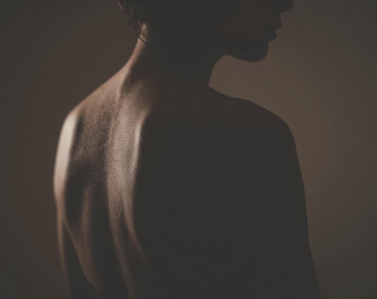 A silhouette of a human form against a dimly lit background, emphasizing the curvature of the back and shoulder, soft edges, deep shadows, warm lighting using #4C4A48 and #F5F2EF.