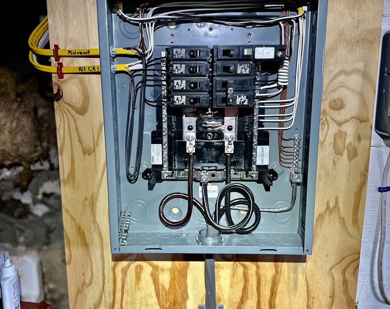 Open electrical breaker panel box with wired circuit breakers mounted on a wooden wall.