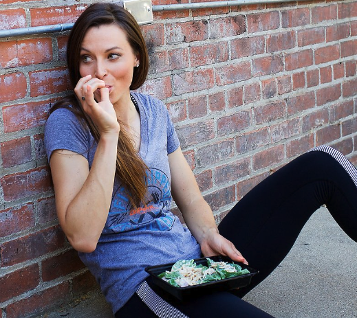 A woman eating some healthy food from a togo container.  