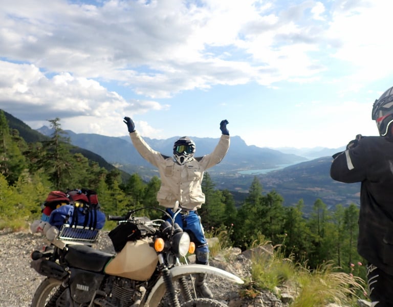 a man standing on a mountain top with his arms up in the air