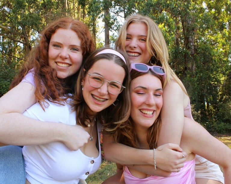 Four smiling women posing for a group photo in a sunny forest setting.