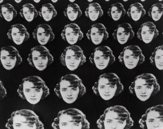 Chorus girls holding multiple large cardboard cutouts of Ruby Keeler’s face against a dark backgroun