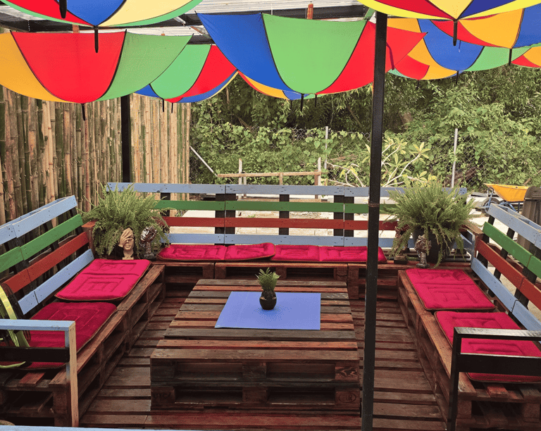Outdoor patio lounge with colorful umbrella ceiling and DIY pallet furniture seating area.