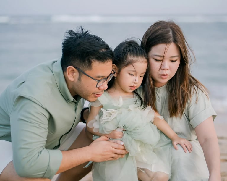 Parents sharing a tender moment with their daughter during a beach family photography session in Bali.