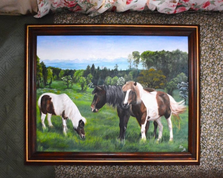 a framed painting of three horses grazing in a field
