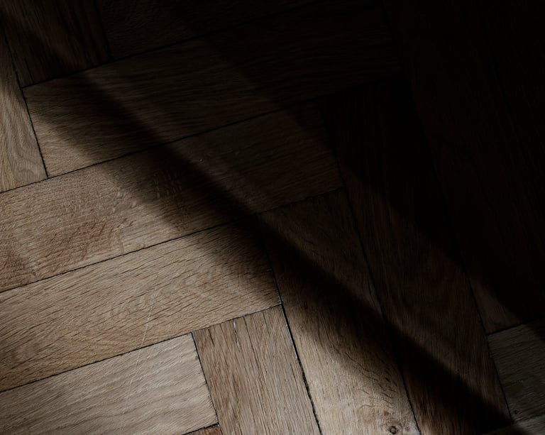 Rustic herringbone oak wood parquet flooring with natural texture and dramatic shadows.
