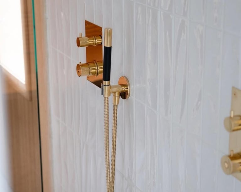 Luxury modern gold shower hardware and handheld sprayer mounted on white textured vertical subway tile.