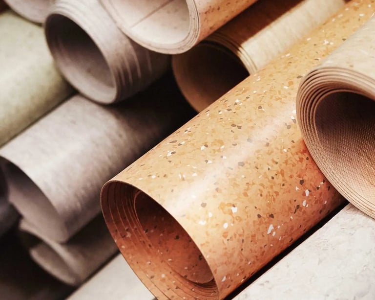 Stacked rolls of durable linoleum flooring in various neutral colors and patterns for home renovation.