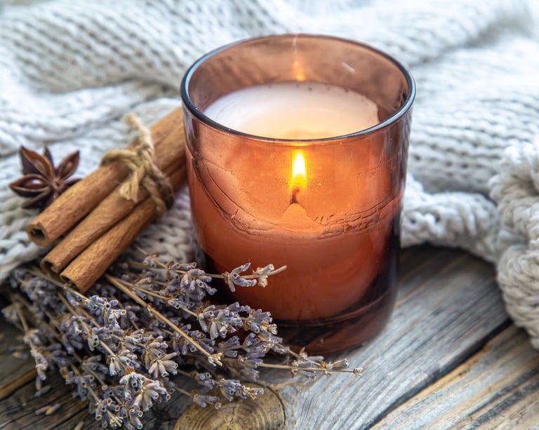 a bundle of lavender, cinnamon sticks and a candle in a glass candle holder, resting on a blanket