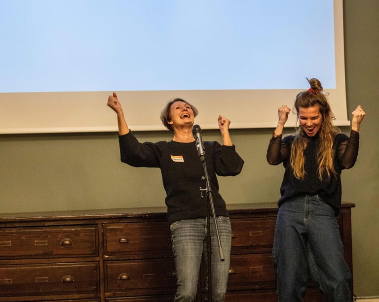 Two women cheering behind a microphone, one public speaking trainer and one participant.
