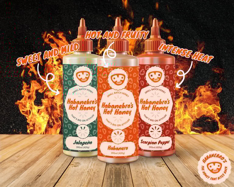 Three squeezy hot honey bottles on a wooden table, with flames in the background.