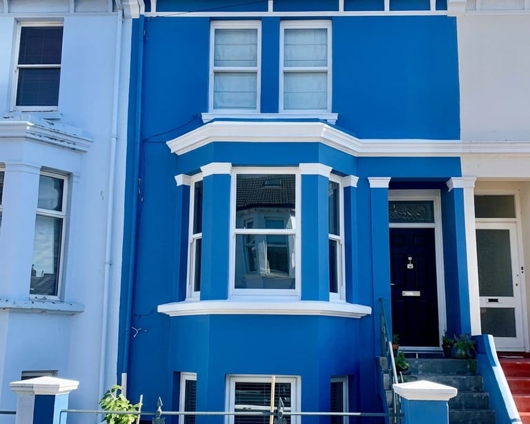 A vibrant blue terraced house with white trim and a large bay window in a residential Brighton area.