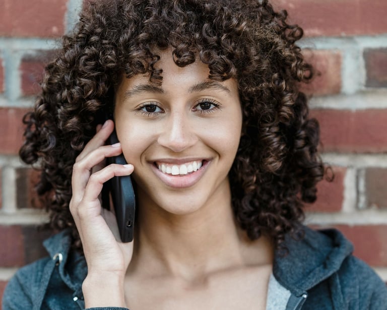 a woman with curly hair and a gray jacket.  She's smiling and talking on the phone.