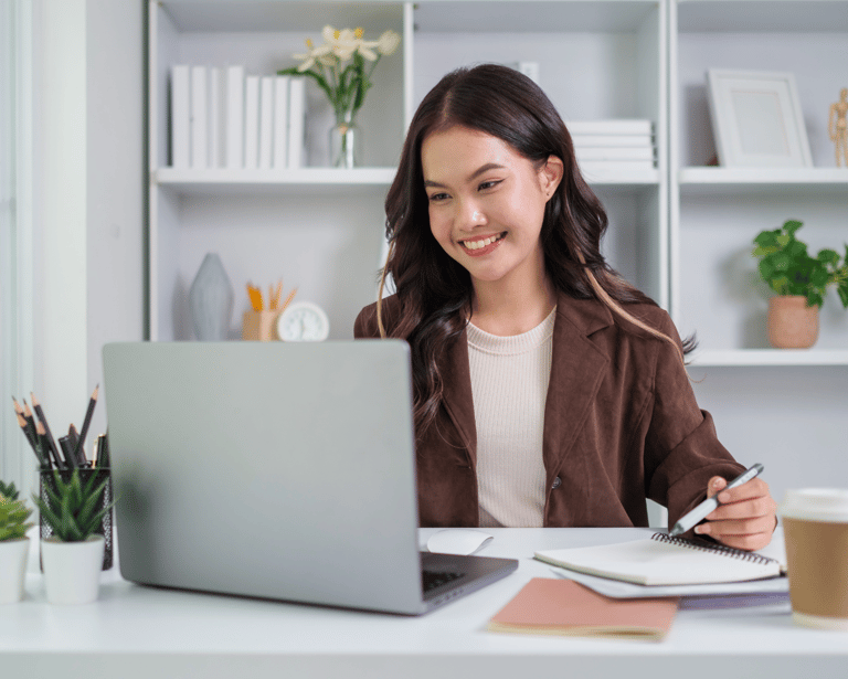 Chica sonriente sentada en un escritorio con un ordenador portátil y una libreta