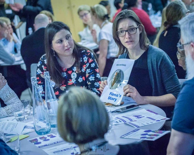 Professional woman holding a Mind and Body case study booklet while networking at a corporate event workshop.