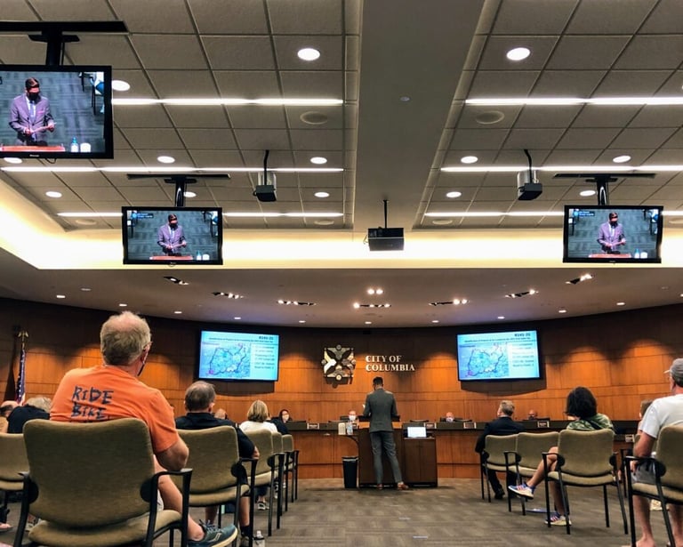 Photo from the back of city council with someone in the center talking at the podium