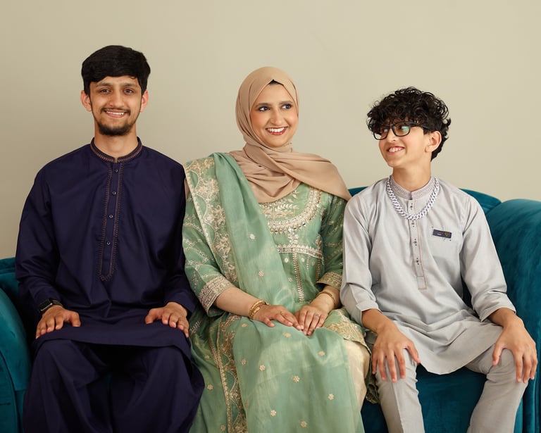A smiling family wearing traditional South Asian Shalwar Kameez and hijab during an Eid celebration.